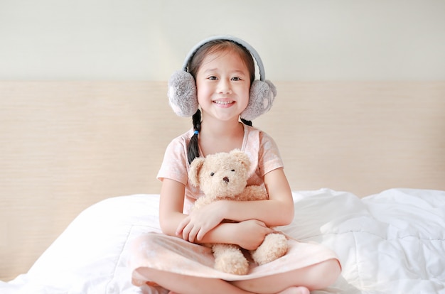 Asian child girl wearing winter earmuffs and embracing teddy bear 