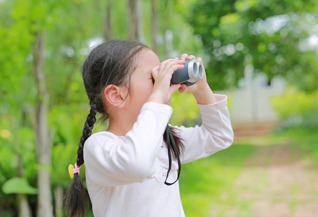 Ragazza asiatica del bambino con il binocolo nei campi della natura