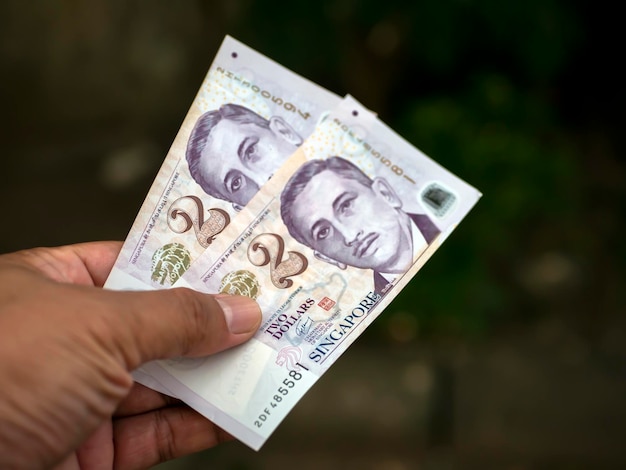 An Asian child holds 2 Singapore dollar banknotes shallow focus