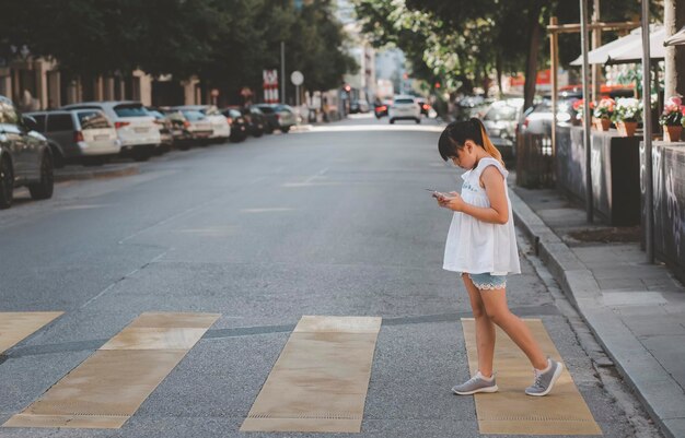 Asian Child is watching the phone on the road crossing or using a mobile phone for a long time hurts her eyes and has an aggressive atmosphere. Concept danger for children's mobile phones.