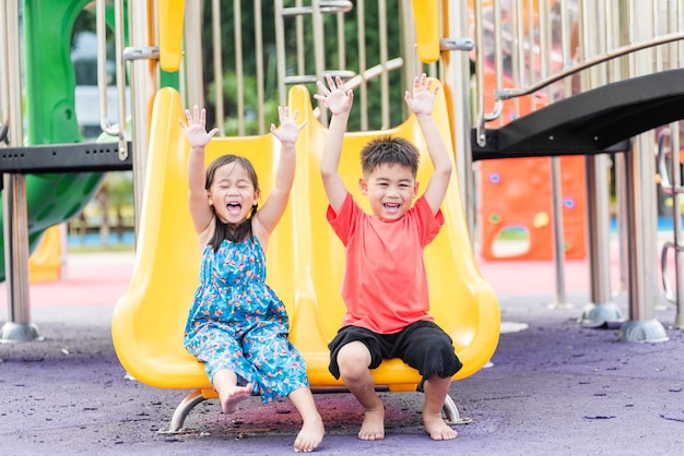 Bambino asiatico sorridente che gioca sul parco giochi all'aperto del giocattolo della barra di scorrimento