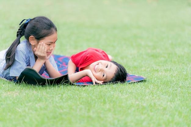 写真 11歳のアジアの子供たちの姉と兄弟は笑顔で楽しんで緑の野原に横たわっています