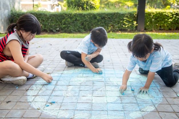 Asian children play outdoors. Child girl draws a planet globe with a map of the world colored chalk on the pavement, asphalt. Earth, peace day concert.