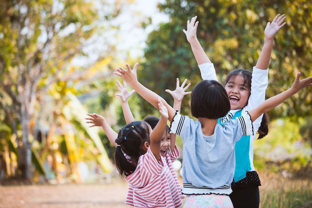 アジアの子供たちが手を挙げ、公園で楽しく遊ぶ