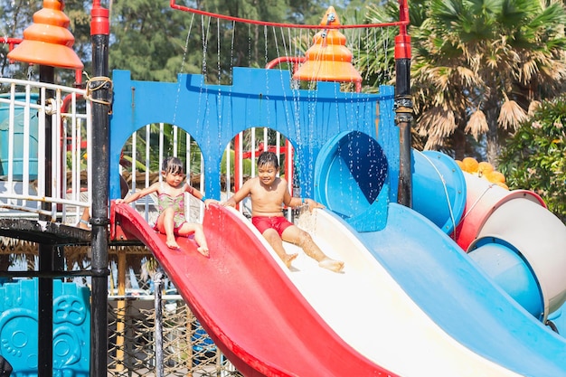 Foto i fratelli asiatici dei bambini nuotano e giocano con il giocattolo della barra di scorrimento dell'acqua nella piscina blu