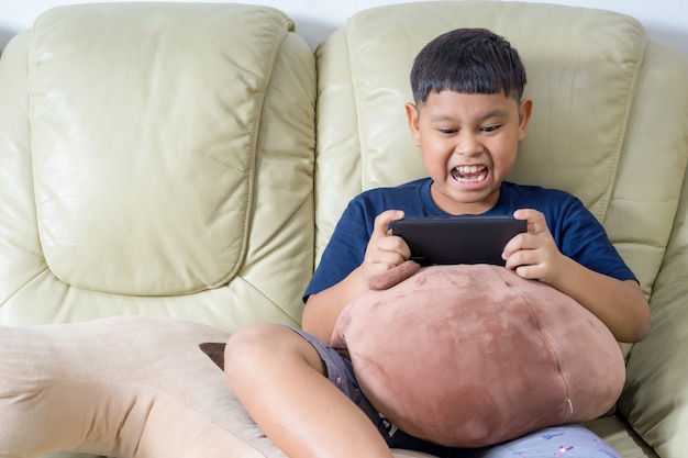 Photo asian children sit on sofa are serious about playing games on mobile phone