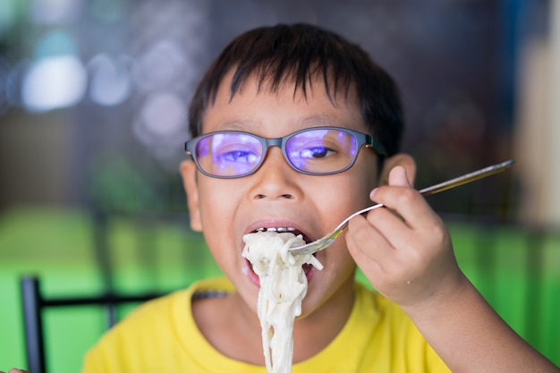 아시아 어린이들은 푸른 빛을 차단하고 식당에서 맛있는 스파게티를 먹는 안경을 착용합니다.