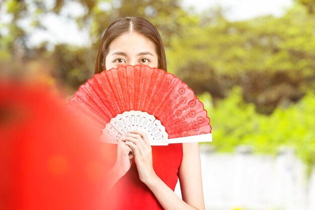 Asian Chinese woman in a cheongsam dress holding fan celebrates Chinese New Year. Happy Chinese New Year