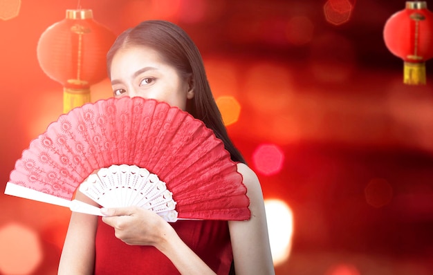 ファンを保持しているチャイナドレスのアジアの中国人女性は、中国の旧正月を祝います。旧正月おめでとう