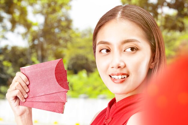 Asian Chinese woman in a cheongsam dress holding red envelopes. Happy Chinese New Year