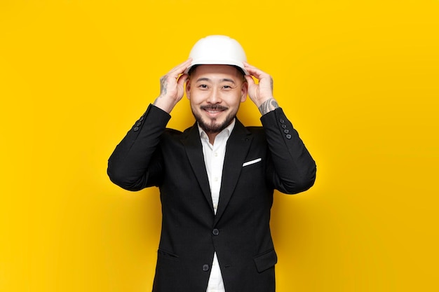 Asian civil engineer in suit holds papers with blueprints on yellow isolated background