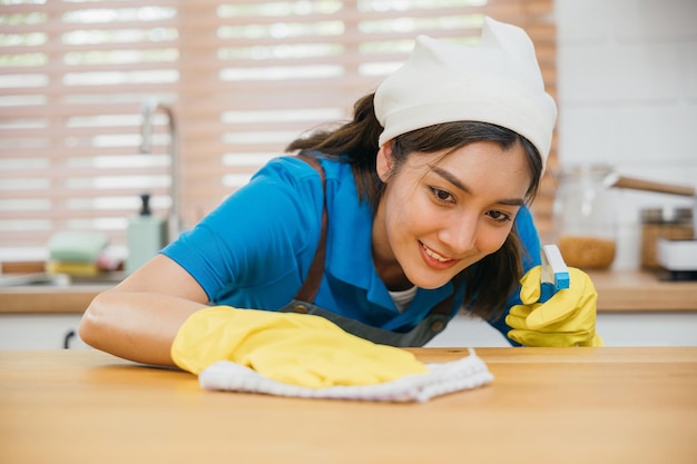 Азиатский специалист по уборке в желтых перчатках вытирает кухонный столик жидким спреем.