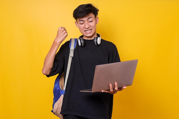 Asian college student holding laptop while clenching fist celebrate success