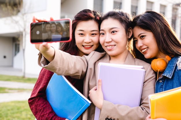Азиатские студенты колледжа делают селфи на мобильный телефон, стоя за пределами университетского городка