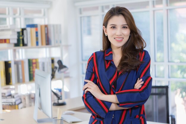 An Asian confident businesswoman is standing with arm crossed and smiling in a working room at home