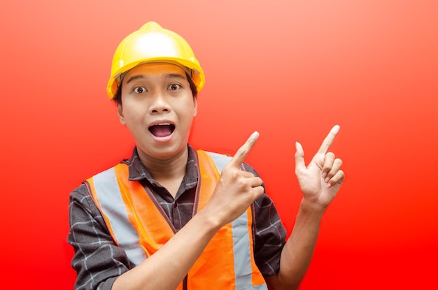 Asian consrtruction worker wearing safety helmet and vest\
pointing finger with shocked expression