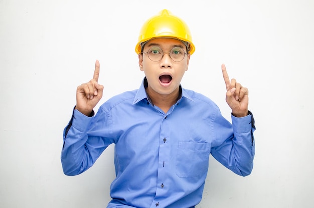 写真 青いシャツと黄色い安全ヘルメットをかぶったアジアの建設労働者が指を差し、提示する