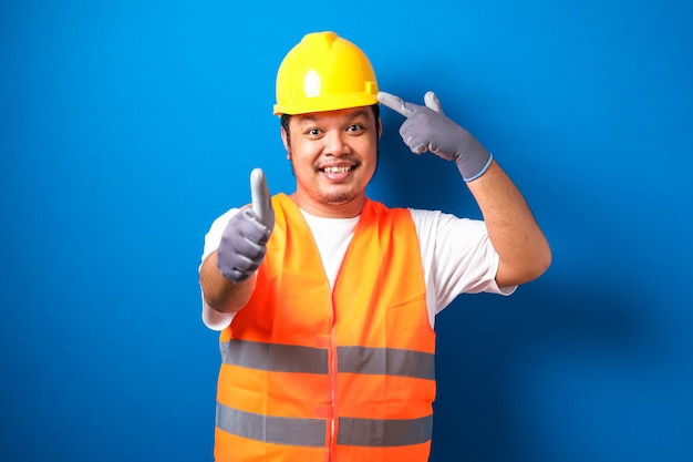 asian construction worker man wearing orange safety vest and helmet over blue background smiling