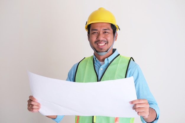 Asian construction worker smiling while holding building design paper