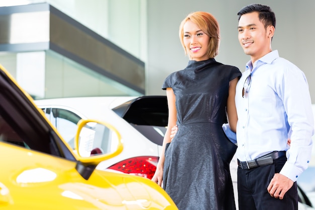 Asian couple choosing luxury sports car in auto dealership looking at a roadster