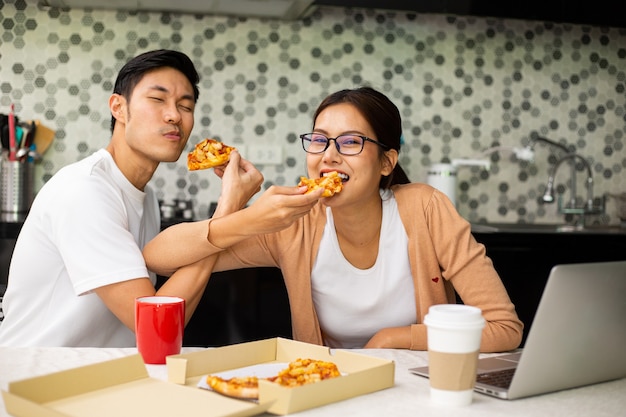 キッチンで一緒にピザを食べるアジアのカップル。健康的な食事をお楽しみください。夕食のライフスタイルと家にいる。インスタントラーメンを食べる女性。