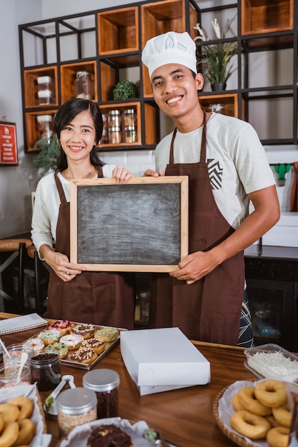 Asian couple holding a blackboard while standing in the kitchen