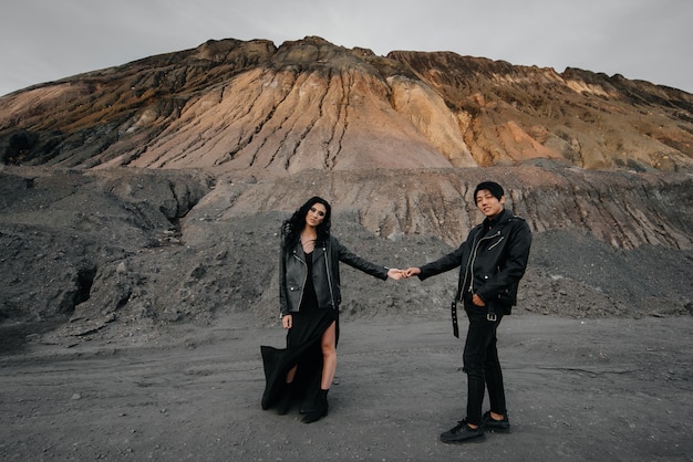 An Asian couple in love in black leather clothes walk in nature among the trees. Style, fashion, love