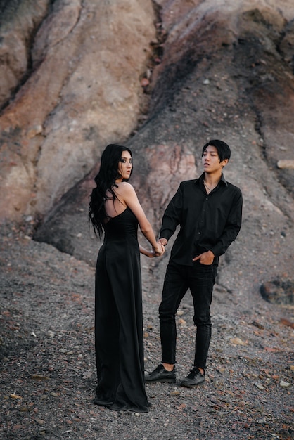An Asian couple in love in black leather clothes walk in nature among the trees. Style, fashion, love