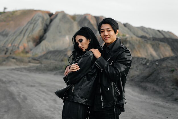 An Asian couple in love in black leather clothes walk in nature among the trees. Style, fashion, love