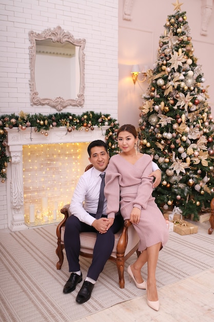 Asian couple in love in elegant outfits celebrate Christmas by the fireplace and tree in luxury home