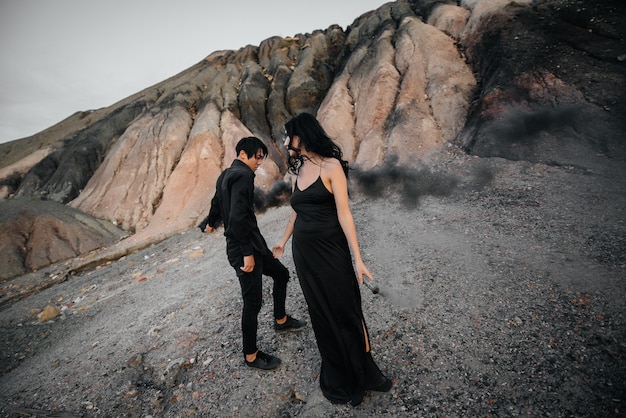 An Asian couple in love lit black smoke bombs in the mountains. Colored smoke