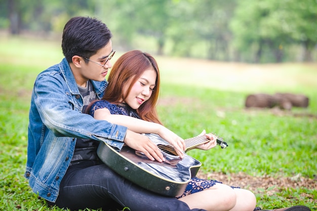 Asian couple in love playing acoustic song  guitar sitting on grass in the park