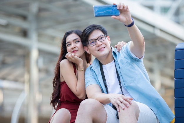 アジアのカップルの愛は通りで携帯電話で写真を撮る