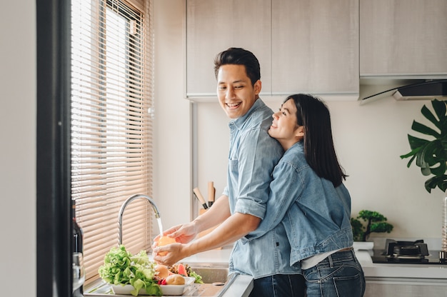 Gli amanti asiatici delle coppie abbracciano nella cucina mentre cucinano a casa