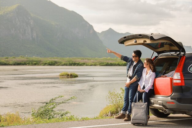 Photo asian couple man with vintage camera and woman sitting on back of car  travel to mountain and lake in holiday with car road trip