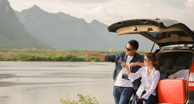 アジアカップルビンテージカメラと車の後ろに座っている女性を持つ男は、車の道旅行と休日に山と湖に旅行します。