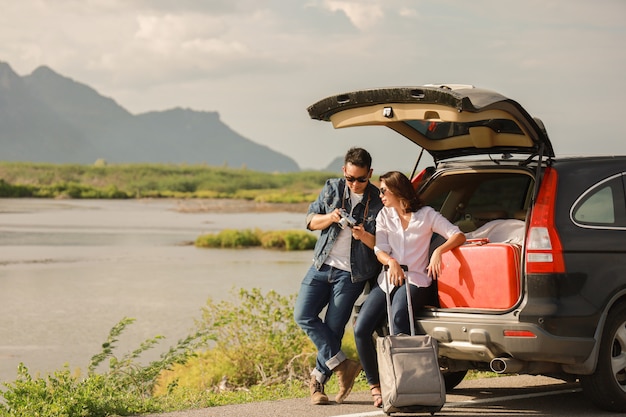 Asian couple Man with vintage camera and woman sitting on back of car  travel to mountain and lake in holiday with car road trip 