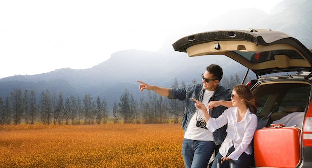 Asian couple Man with vintage camerra and woman sitting on back of car 