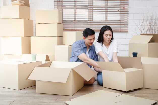 Asian couple moving into a new home Help unpack the brown paper box to decorate the house. Concept of starting a new life, building a family. Copy space