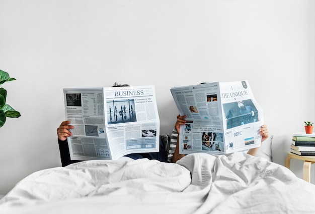 Фото Азиатская пара, читающая газеты в постели