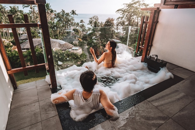 Asian Couple relaxing in outdoor bath with tropical sea luxury spa hotel, lifestyle concept