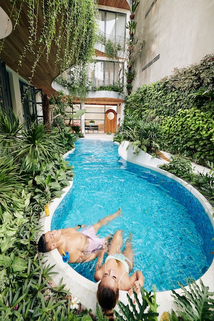 Asian couple relaxing in swimming pool of spa hotel and enjoying hydrotherapy, romantic getaway concept