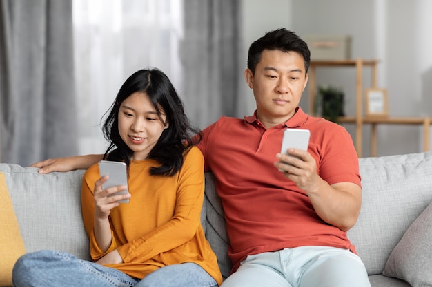 Coppia asiatica seduta sul divano insieme utilizzando i loro smartphone