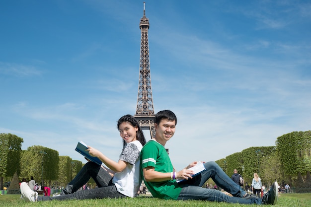 Il libro di lettura asiatico dell'allievo delle coppie insieme all'aria aperta parcheggia vicino alla torre eiffel a parigi, francia.