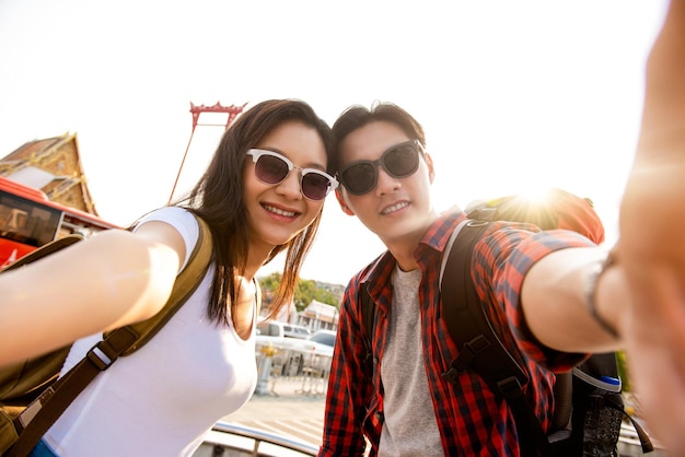 Asian couple tourists taking selfie while traveling on summer vacations in Bangkok Thailand