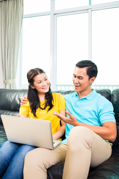 Asian couple using laptop on sofa