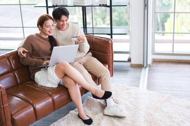 Photo asian couple wearing sweaters with a laptop man uses a credit card to pay on the website