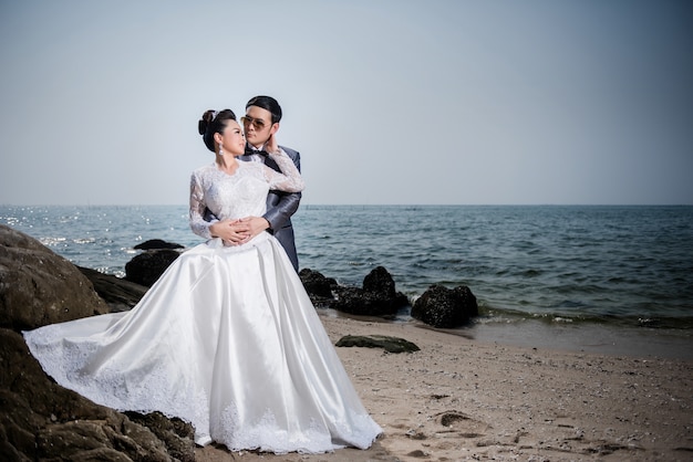 해변 결혼식을위한 웨딩 드레스와 양복을 입고 아시아 부부