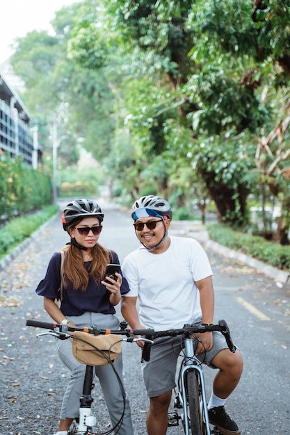 携帯電話でヘルメットをかぶったアジア人カップルが自転車に乗って幸せそう