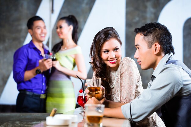 Asian couples flirting and drinking at nightclub bar 